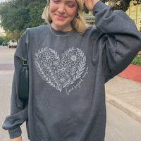 Person wearing a gray sweatshirt with a floral heart design outdoors.