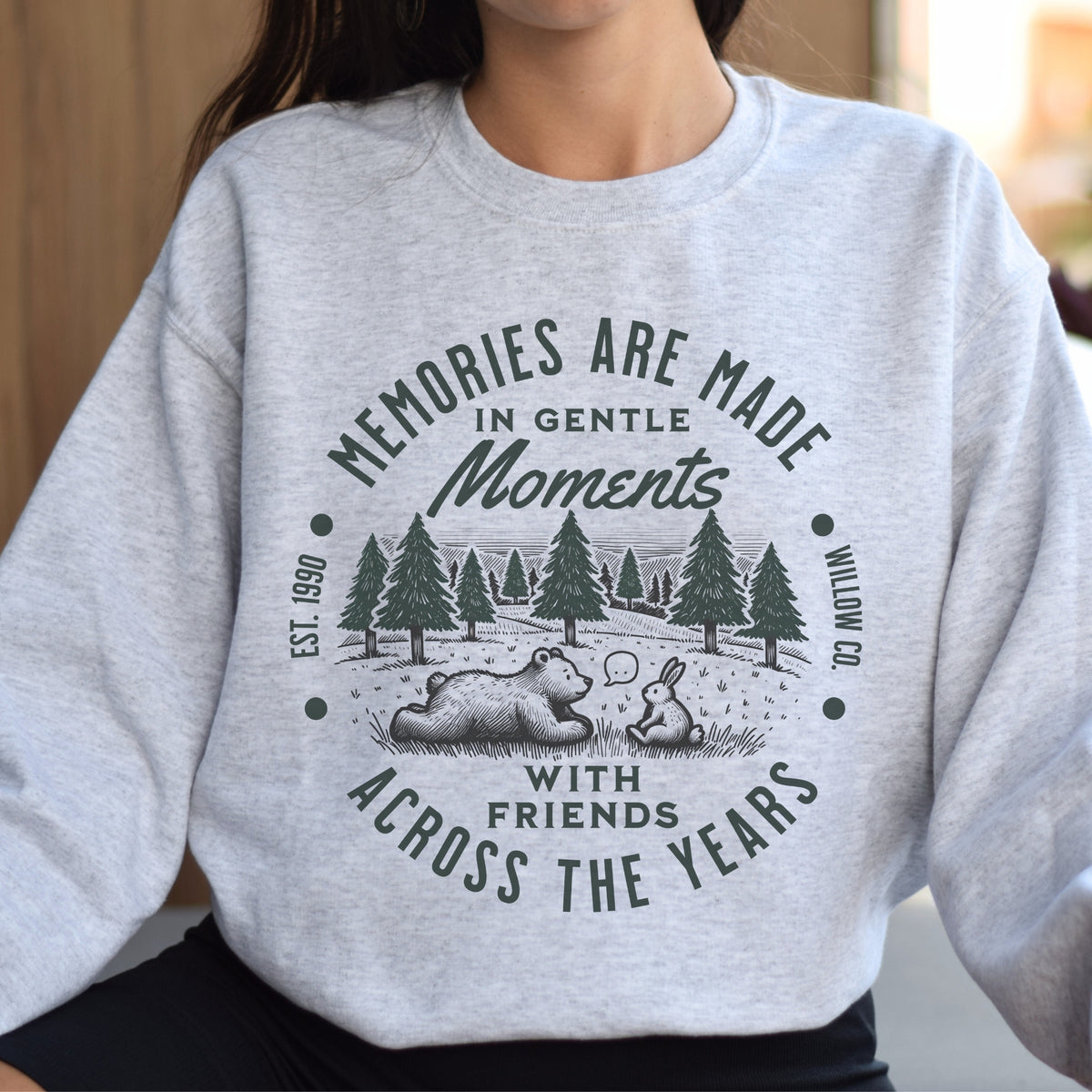 Gray sweatshirt with a graphic design and text 'Memories are made in gentle moments with friends across the years'.
