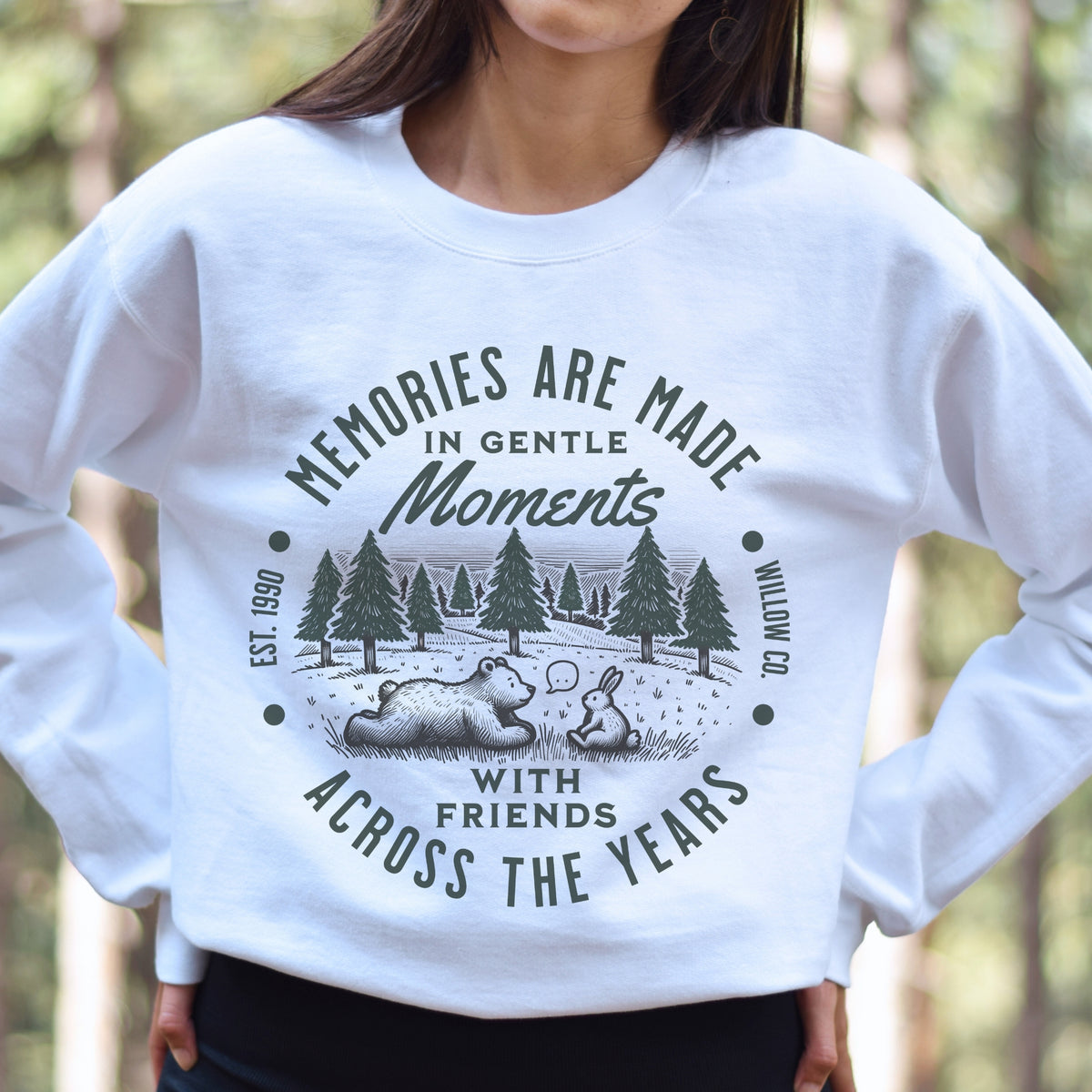 White sweatshirt with nature-themed design and text in a forest setting