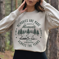Person wearing a beige sweatshirt with a nature-themed design in a forest setting