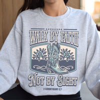 Gray sweatshirt with a graphic of a cowboy boot and text 'Walk by Faith Not by Sight' on a blurred background.