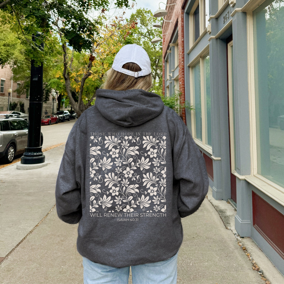 Person wearing a dark hoodie with a floral design and text on the back, walking down a street.