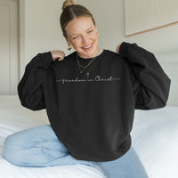 Woman wearing a black sweatshirt with 'freedom in Christ' text, sitting on a bed.