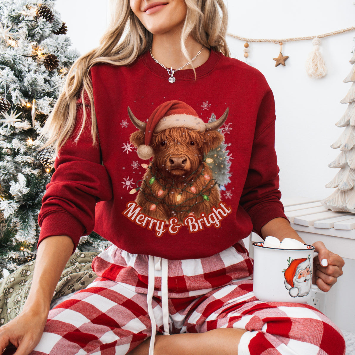 Person wearing a red Christmas-themed sweater with a Highland cow design, sitting by a decorated Christmas tree.