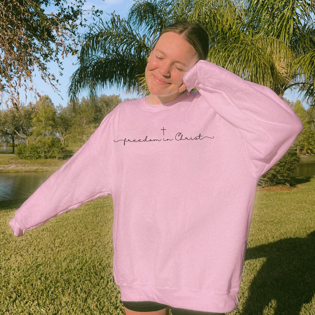 Person wearing a pink sweatshirt with 'freedom in Christ' text outdoors.