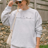 Person wearing a gray sweatshirt with 'freedom in Christ' text, standing in front of a stone wall.