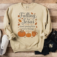 Beige sweatshirt with 'Falling for Jesus (and pumpkin everything)' text on a wooden surface with shoes and jeans.