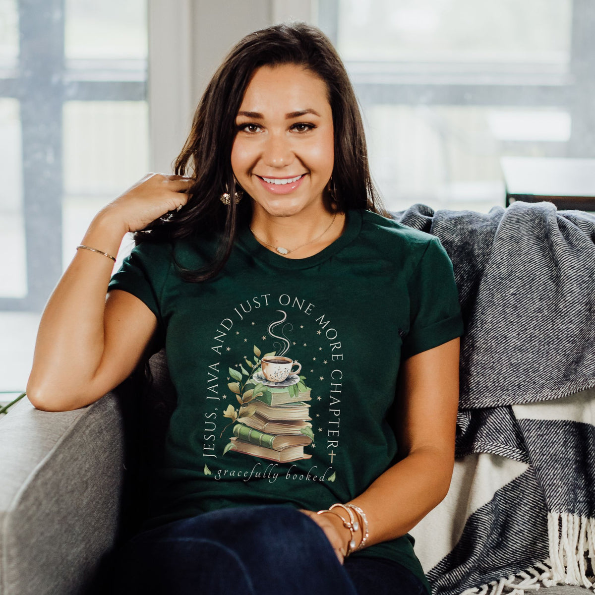 Woman wearing a green t-shirt with a book-themed design, sitting on a couch.