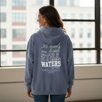 Person wearing a blue hoodie with text on the back, standing in front of a window with cityscape view.