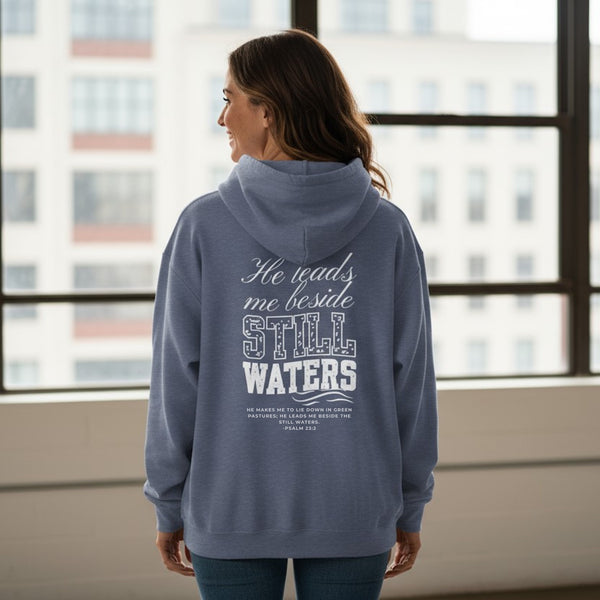 Person wearing a blue hoodie with text on the back, standing in front of a window with cityscape view.