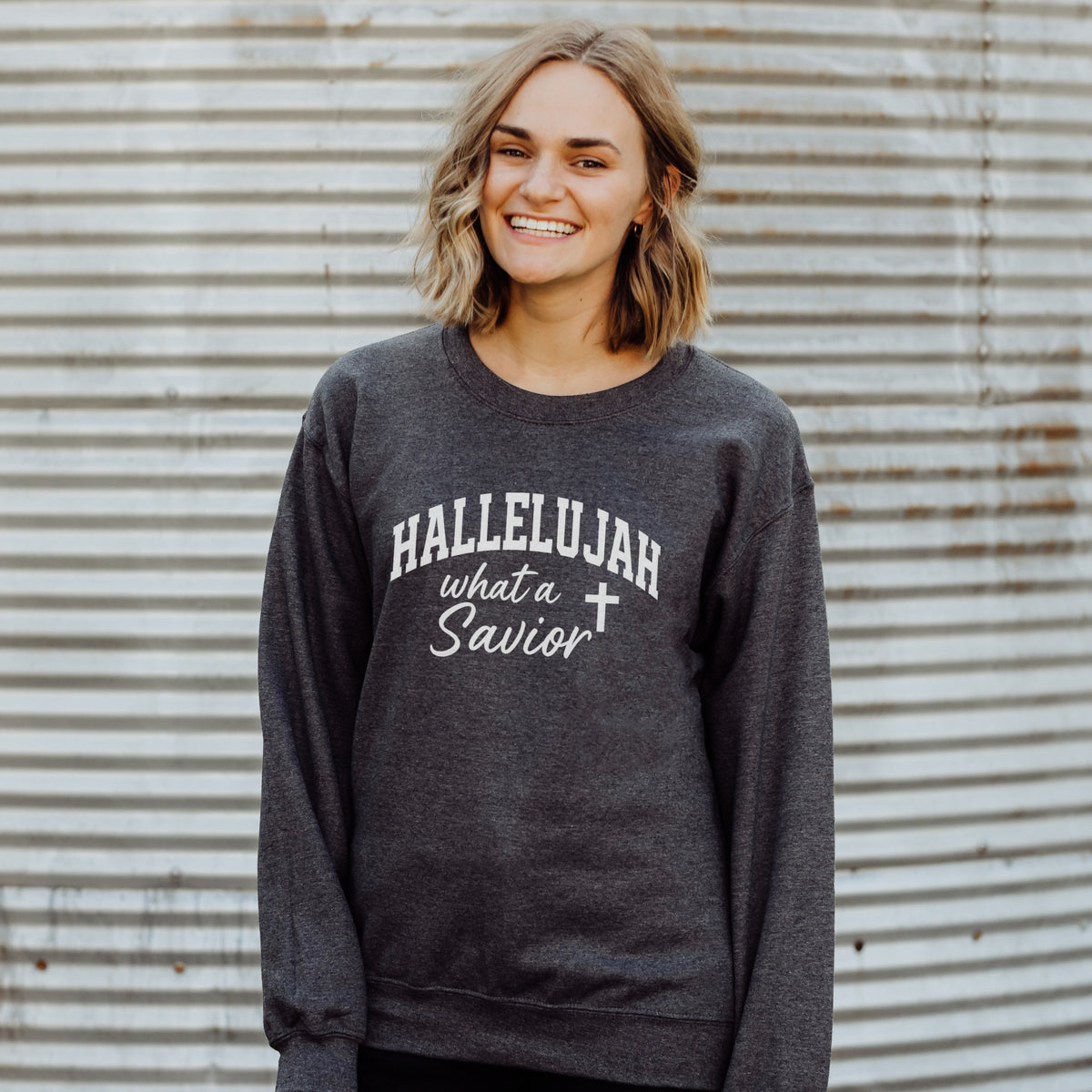 Person wearing a dark gray sweatshirt with 'HALLELUJAH what a Savior' text against a corrugated metal background