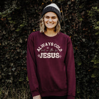 Person wearing a maroon sweatshirt with text standing against a leafy background