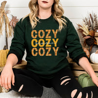 Person wearing a green sweatshirt with 'COZY COZY COZY' text in a fall-themed setting.