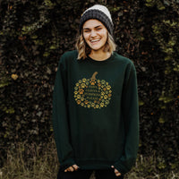 Person wearing a green sweatshirt with a pumpkin design and text, standing against a textured wall.