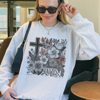 Person wearing a gray sweatshirt with floral and cross design, sitting indoors.