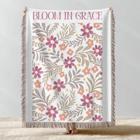Floral patterned throw blanket with 'Bloom in Grace' text on a plain background